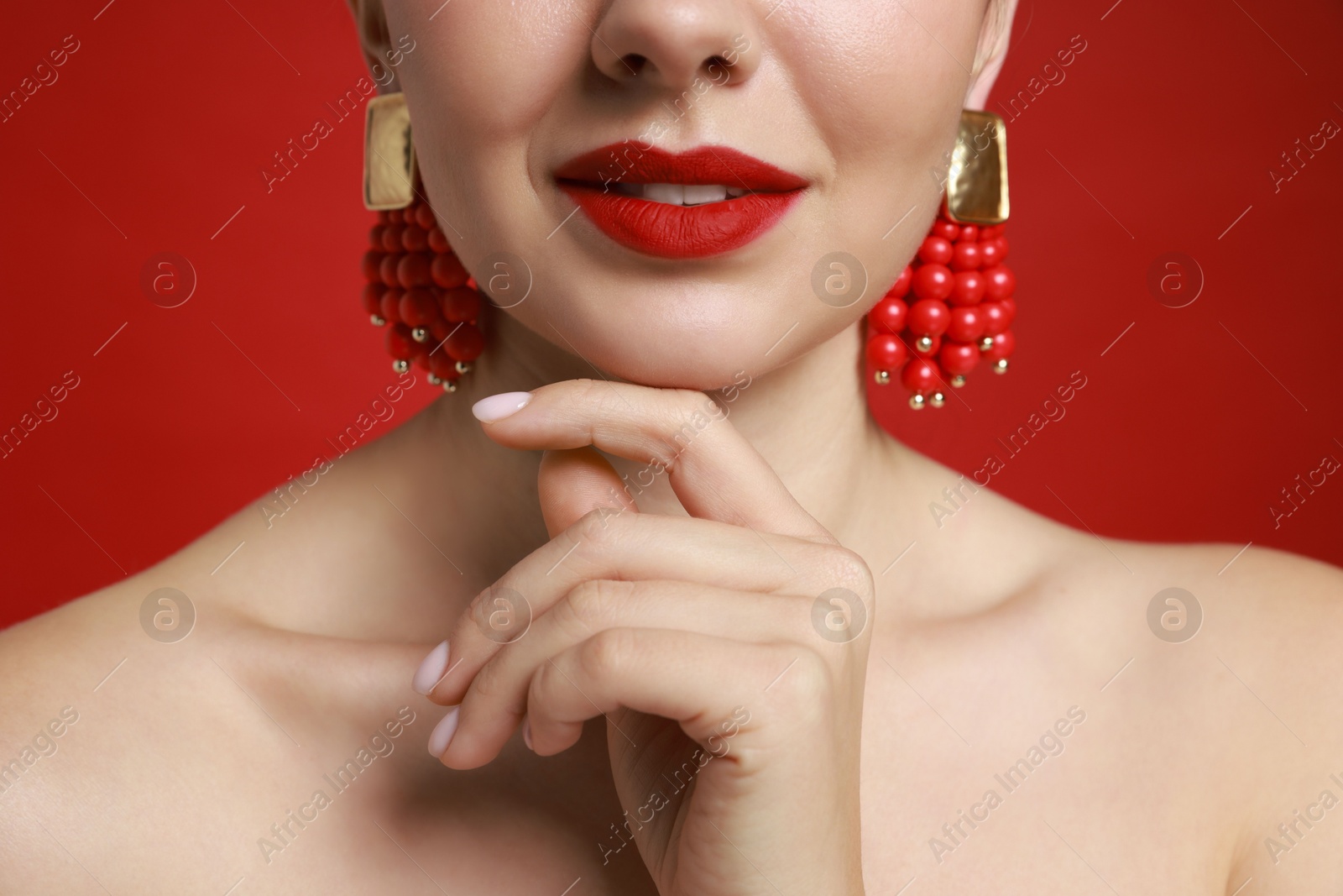 Photo of Beautiful young woman wearing elegant earrings on red background, closeup