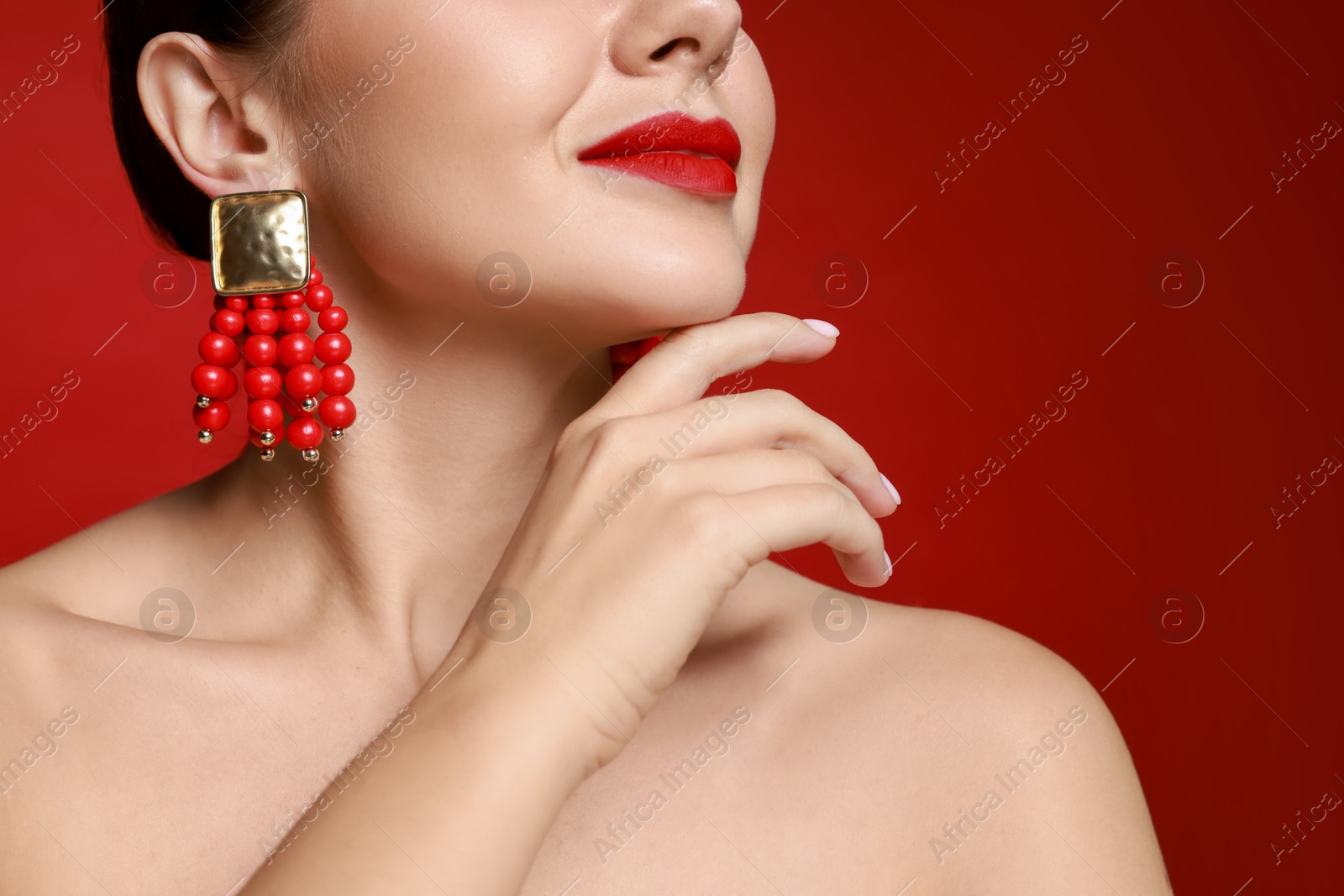 Photo of Beautiful young woman wearing elegant earrings on red background, closeup. Space for text