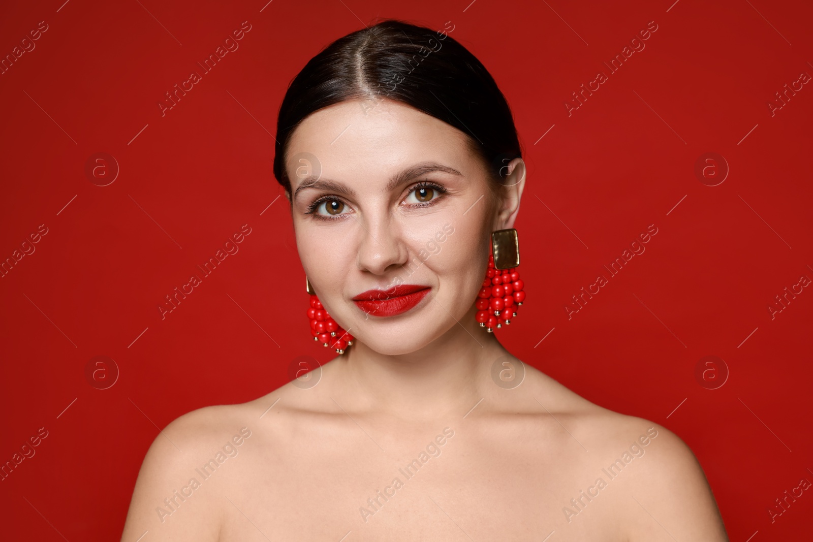 Photo of Beautiful young woman wearing elegant earrings on red background