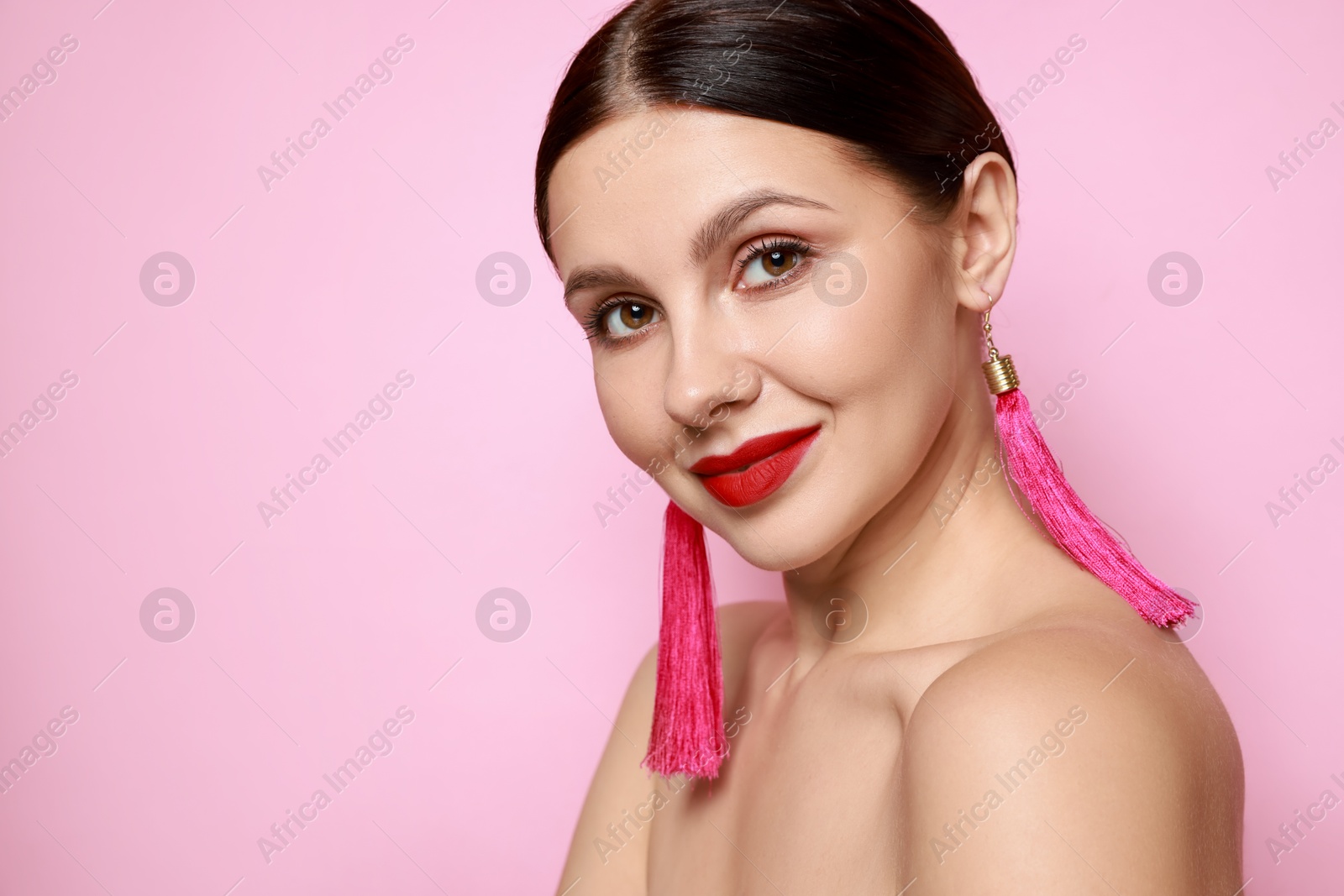 Photo of Beautiful young woman wearing stylish earrings on pink background. Space for text