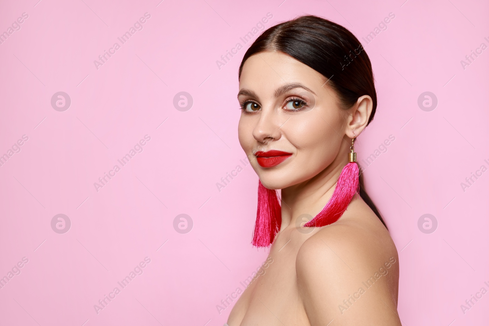 Photo of Beautiful young woman wearing stylish earrings on pink background. Space for text