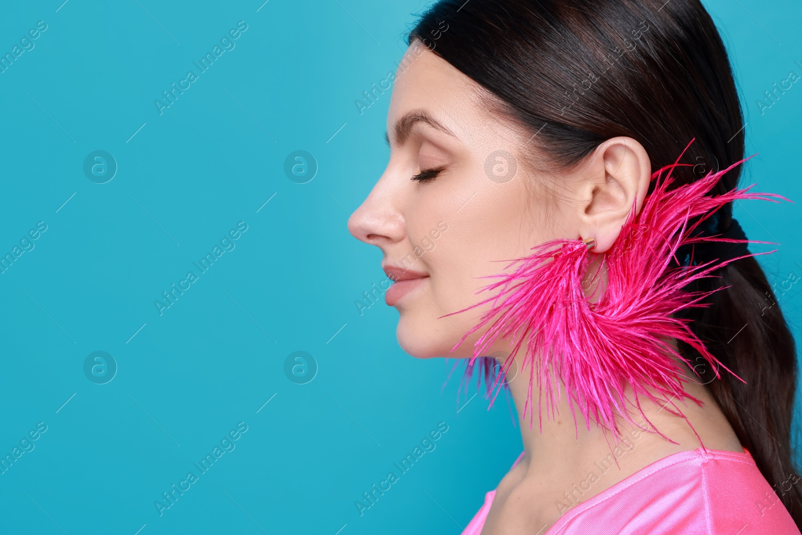 Photo of Beautiful young woman wearing stylish earrings on light blue background, closeup. Space for text