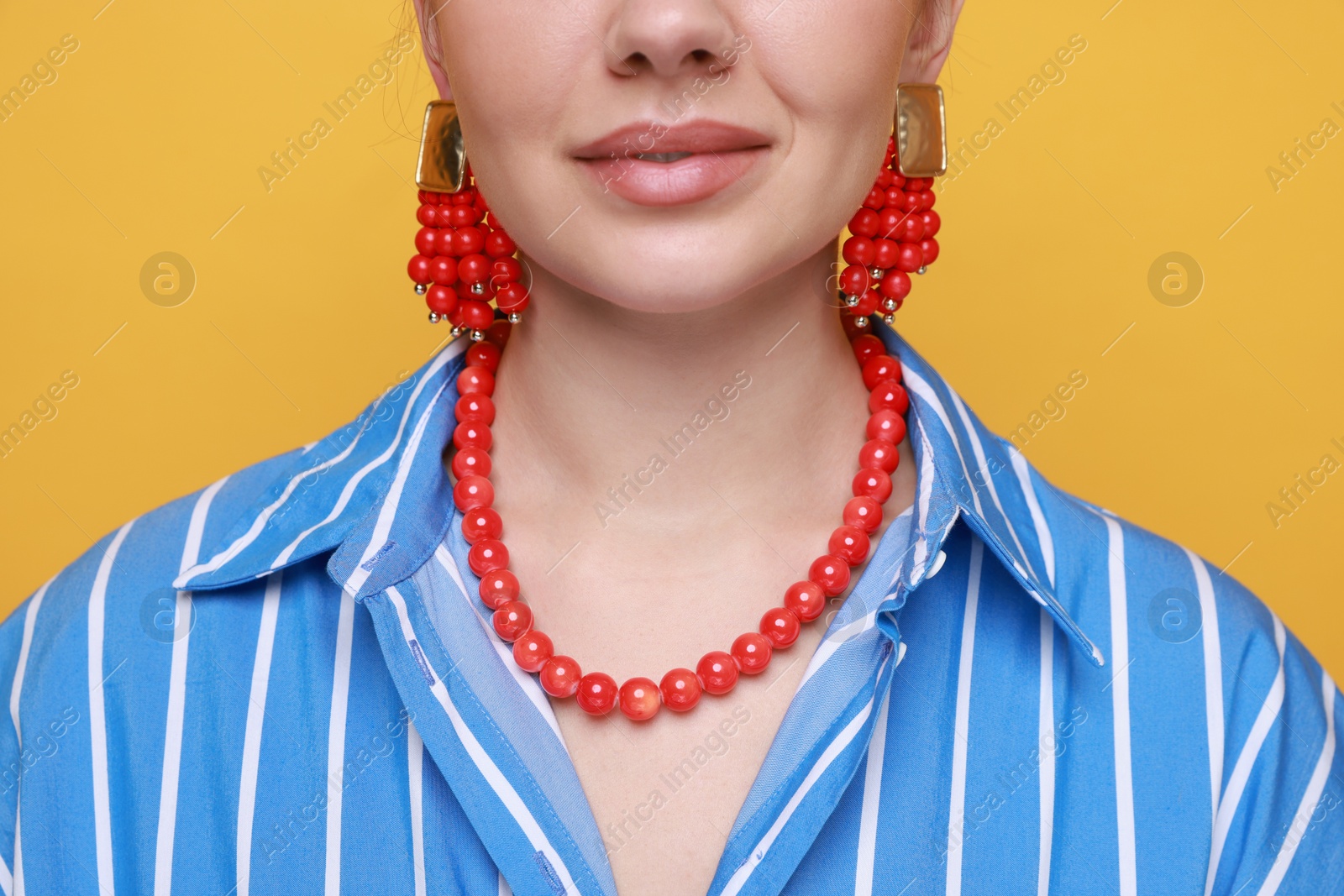 Photo of Young woman wearing stylish earrings and necklace on orange background, closeup