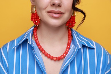 Young woman wearing stylish earrings and necklace on orange background, closeup