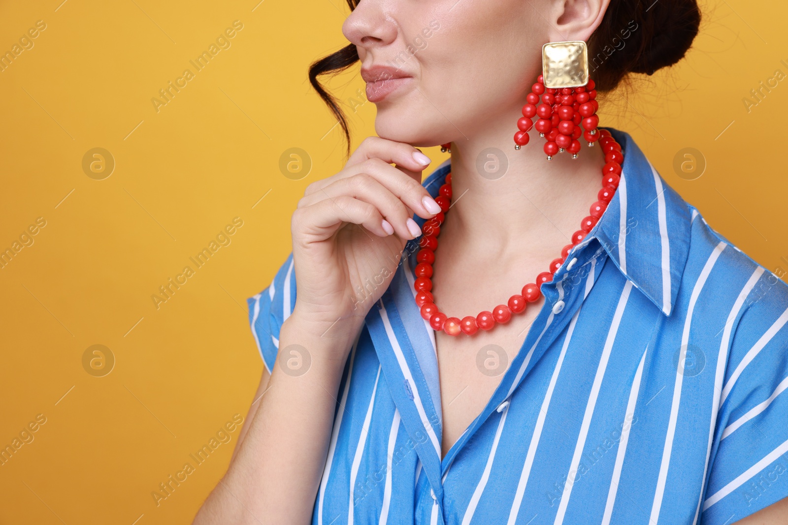 Photo of Young woman wearing stylish earrings and necklace on orange background, closeup. Space for text