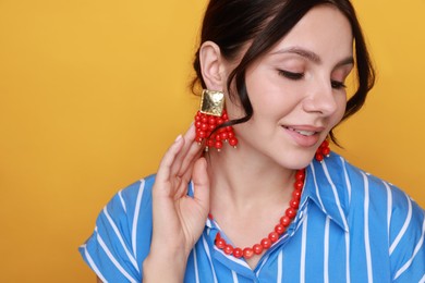 Photo of Young woman wearing stylish earrings and necklace on orange background, closeup. Space for text