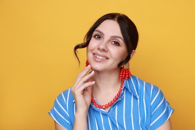 Photo of Young woman wearing stylish earrings and necklace on orange background, closeup