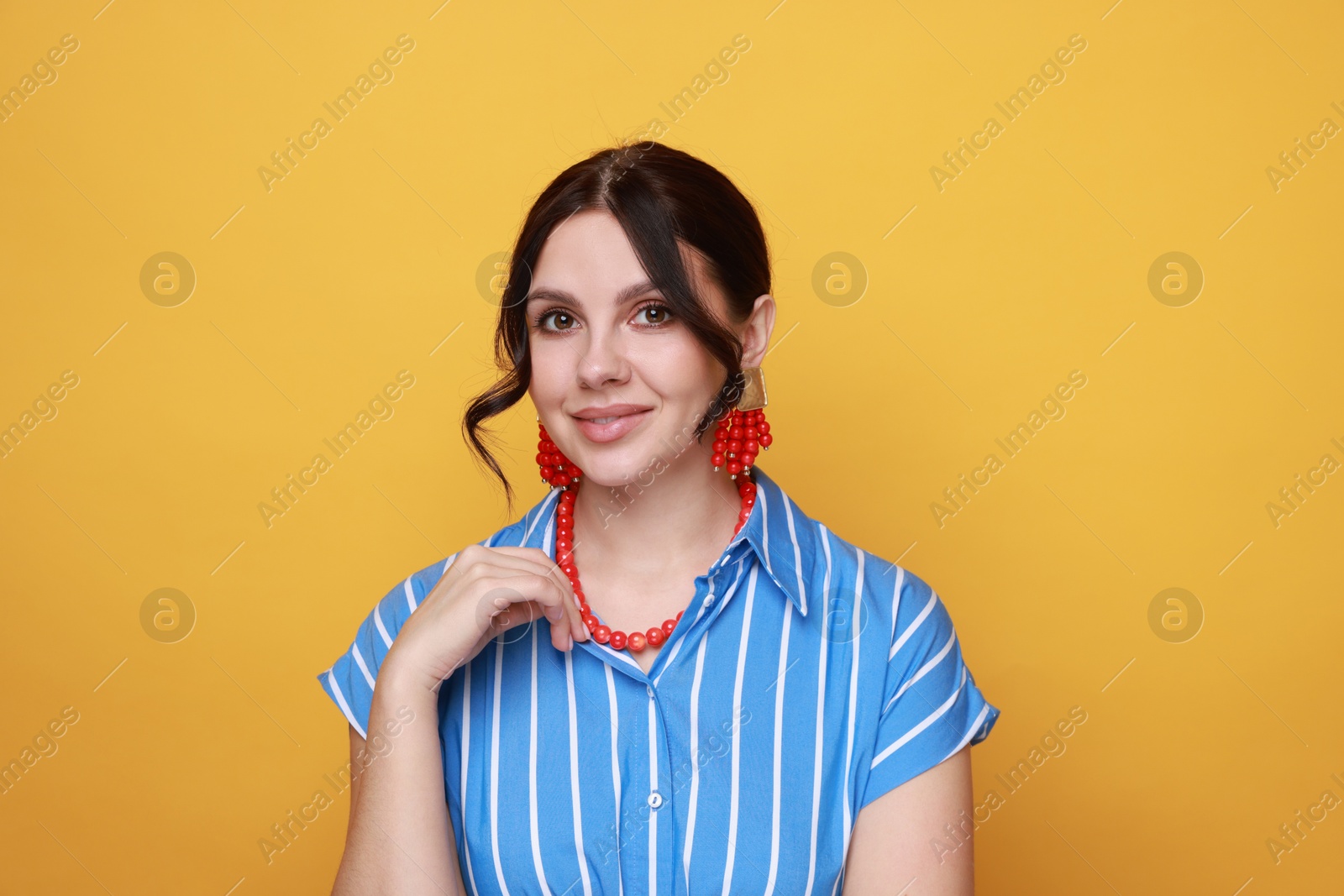 Photo of Young woman wearing stylish earrings and necklace on orange background, closeup