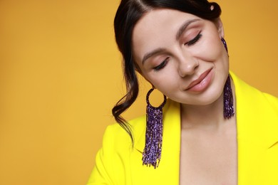 Photo of Beautiful young woman wearing stylish earrings on orange background, closeup. Space for text