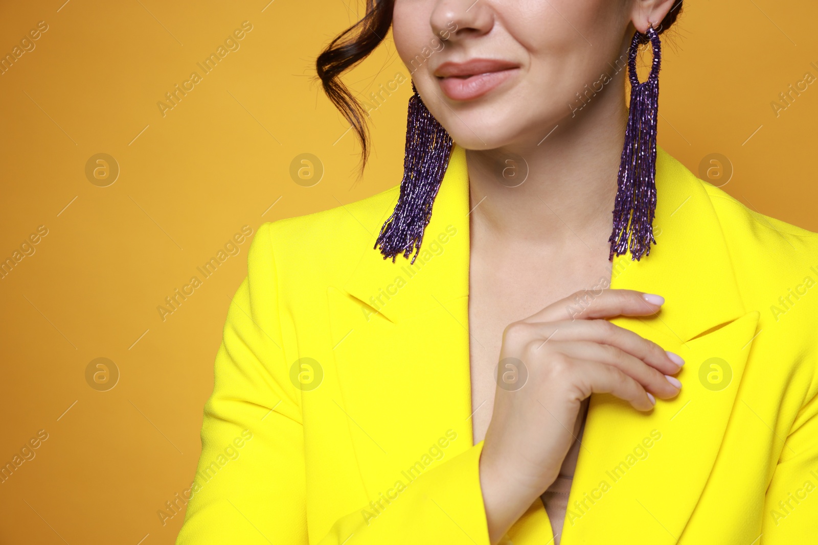 Photo of Woman wearing stylish earrings on orange background, closeup