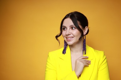 Photo of Beautiful young woman wearing stylish earrings on orange background. Space for text