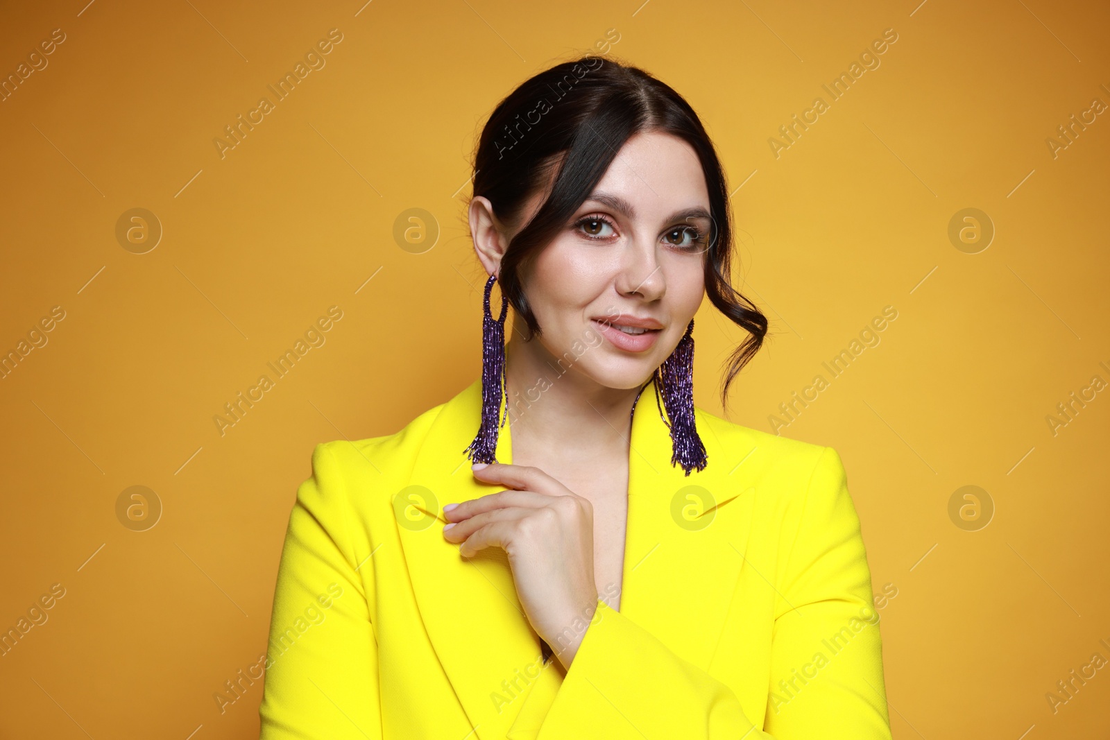 Photo of Beautiful young woman wearing stylish earrings on orange background