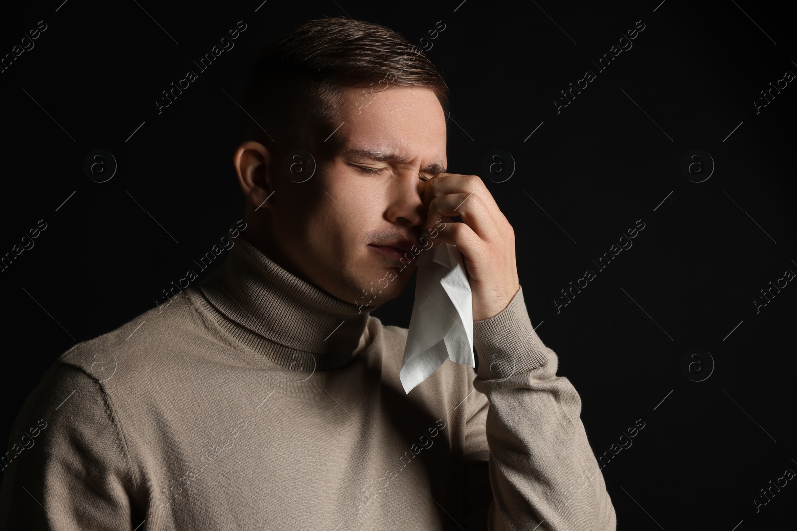 Photo of Crying man wiping tears with tissue on black background