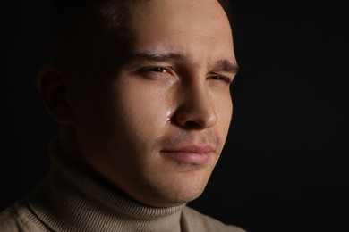 Photo of Distressed young man crying on black background, closeup