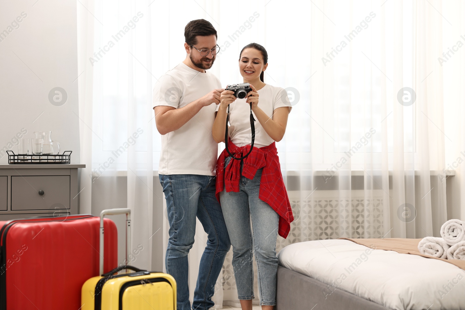 Photo of Happy travellers with camera and suitcases in hotel room