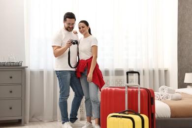 Photo of Happy travellers with camera and suitcases in hotel room