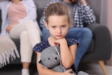 Photo of Resentful little girl with toy and her parents at home. Family dispute