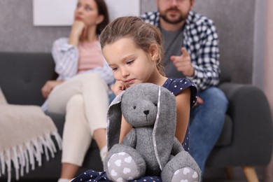 Photo of Resentful little girl with toy and her parents at home. Family dispute