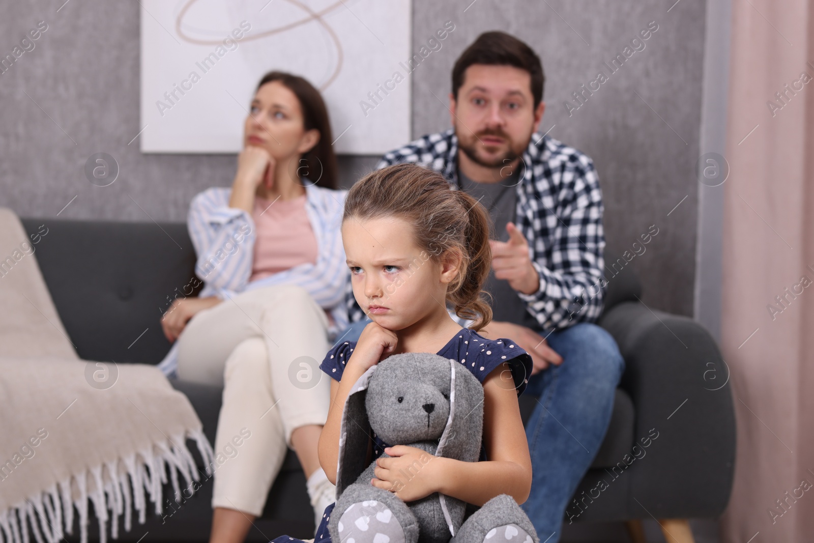 Photo of Resentful little girl with toy and her parents at home. Family dispute