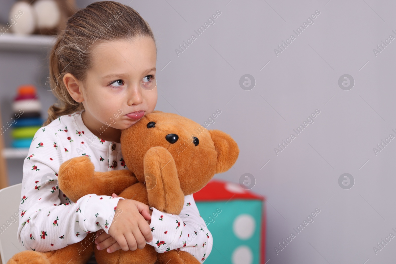 Photo of Resentful little girl with teddy bear at home, space for text