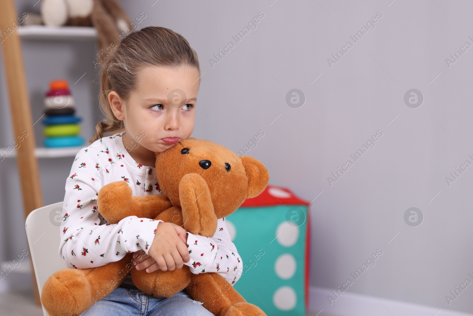 Photo of Resentful little girl with teddy bear at home, space for text