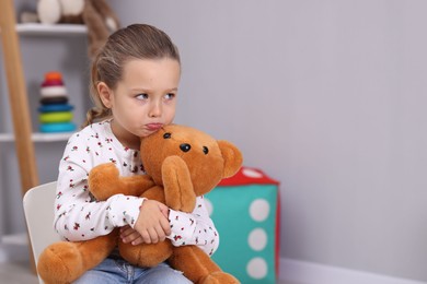 Photo of Resentful little girl with teddy bear at home, space for text