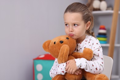 Photo of Resentful little girl with teddy bear at home, space for text