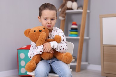 Photo of Resentful little girl with teddy bear at home