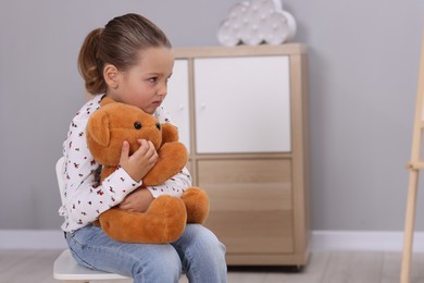 Photo of Resentful little girl with teddy bear at home, space for text