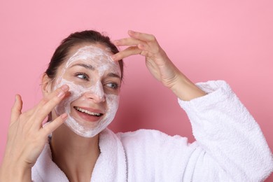 Photo of Spa day. Beautiful woman applying mask onto her face on pink background