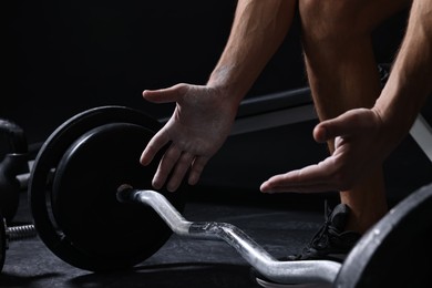 Photo of Man clapping hands with talcum powder before training with barbell in gym, closeup