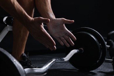 Man clapping hands with talcum powder before training with barbell in gym, closeup