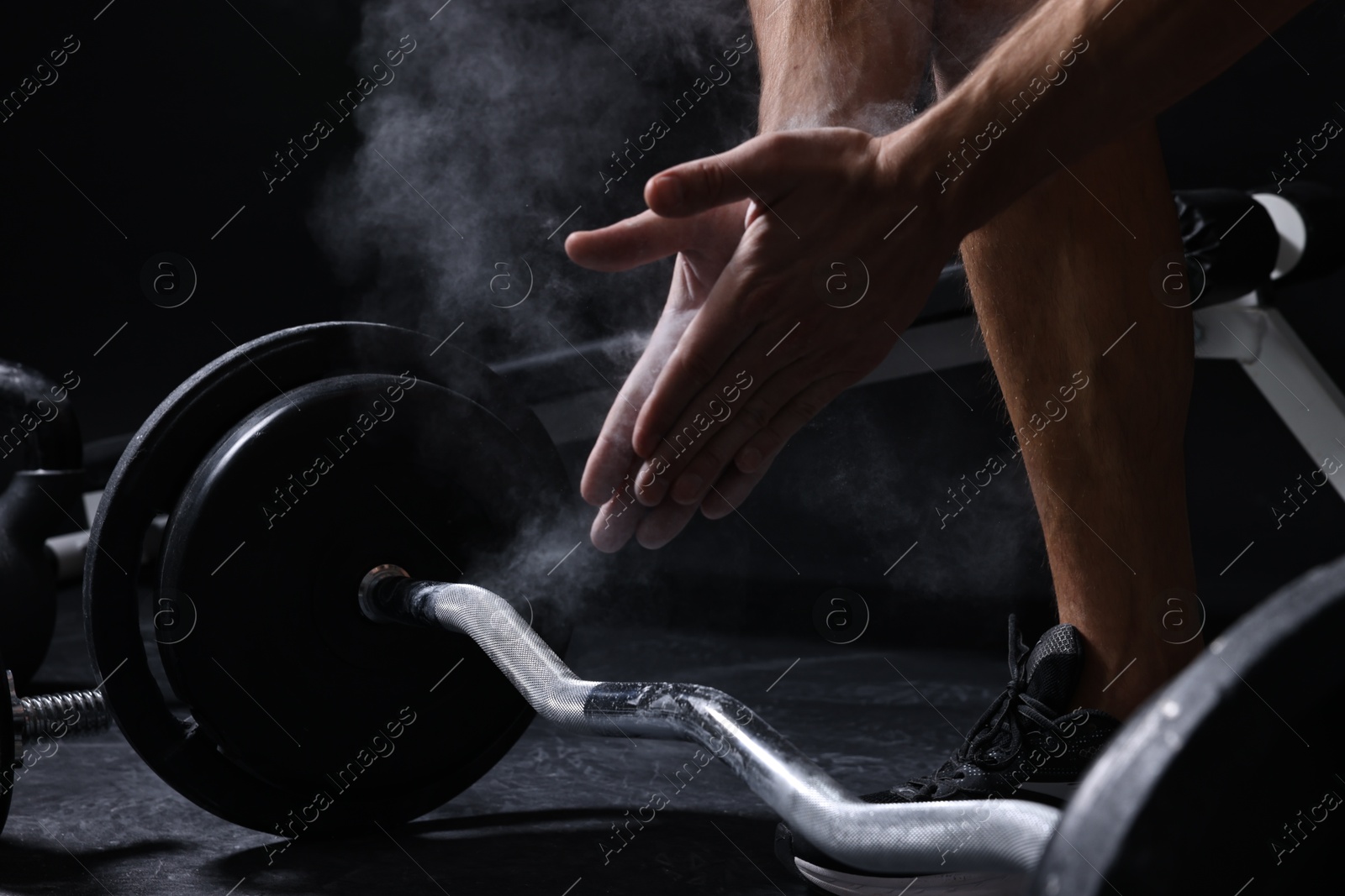 Photo of Man clapping hands with talcum powder before training with barbell in gym, closeup