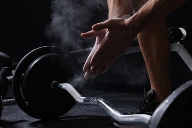 Man clapping hands with talcum powder before training with barbell in gym, closeup