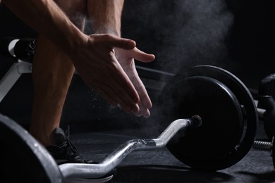 Man clapping hands with talcum powder before training with barbell in gym, closeup