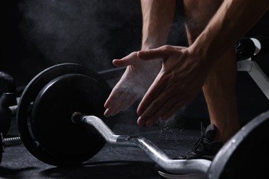 Photo of Man clapping hands with talcum powder before training with barbell in gym, closeup