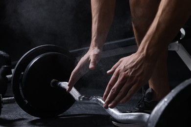 Photo of Man clapping hands with talcum powder before training with barbell in gym, closeup