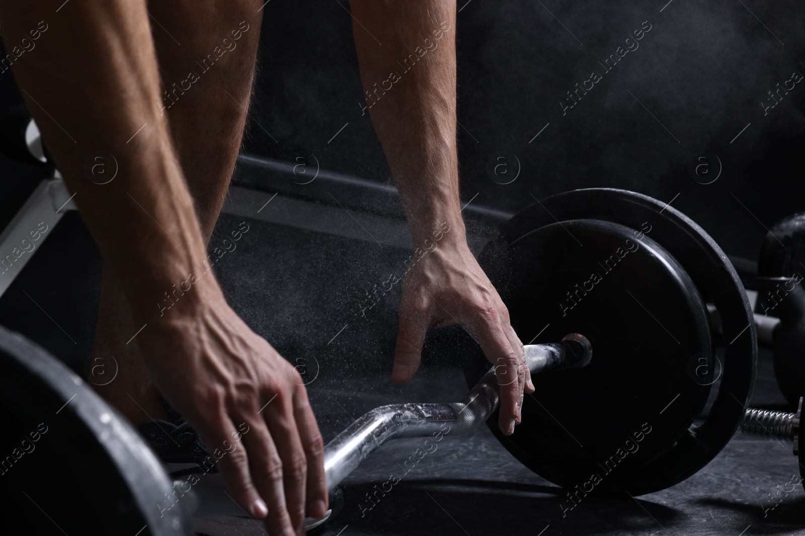 Photo of Man with talcum powder on hands training with barbell in gym, closeup