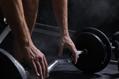 Photo of Man with talcum powder on hands training with barbell in gym, closeup