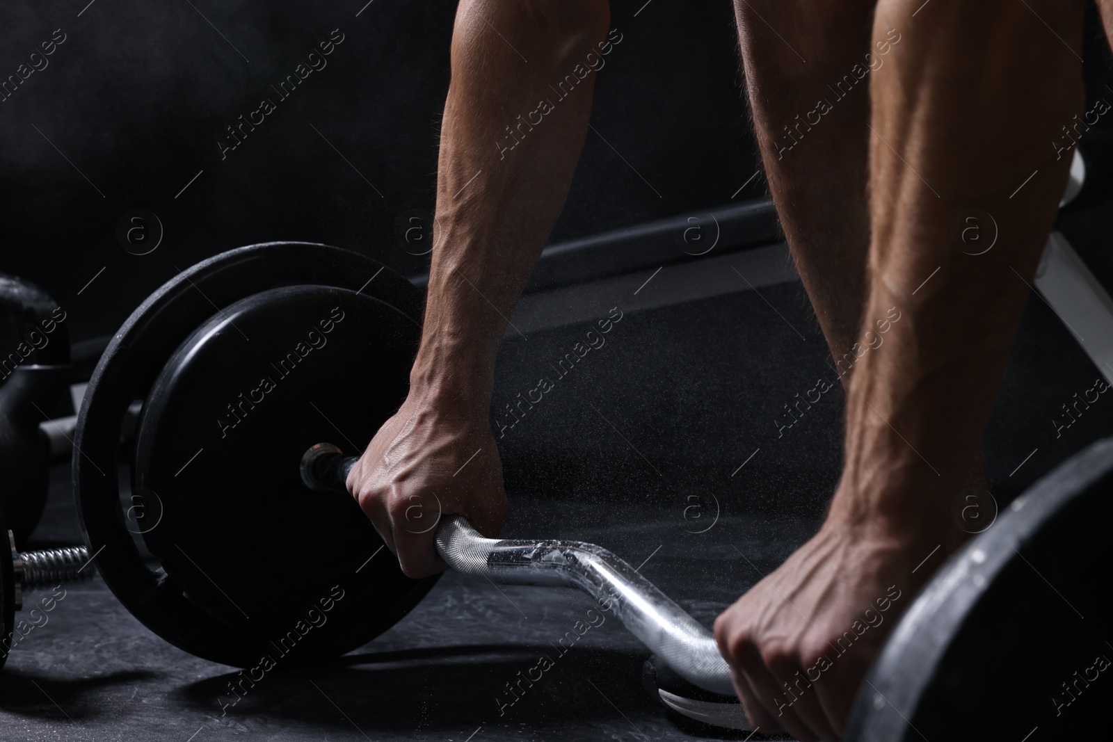 Photo of Man with talcum powder on hands training with barbell in gym, closeup