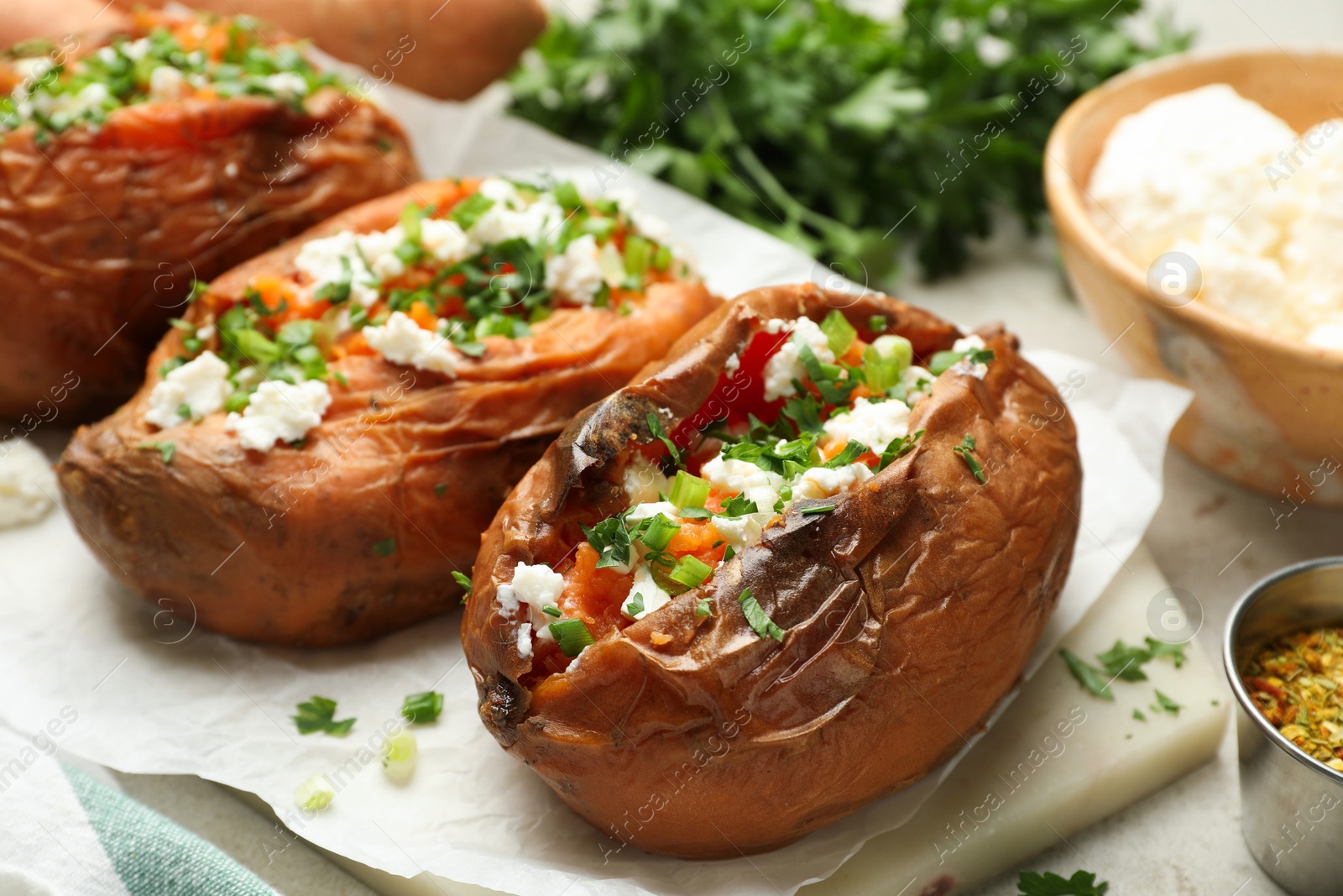 Photo of Tasty cooked sweet potatoes with feta cheese, green onion and parsley on table, closeup