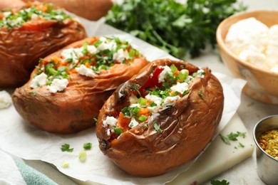 Photo of Tasty cooked sweet potatoes with feta cheese, green onion and parsley on table, closeup