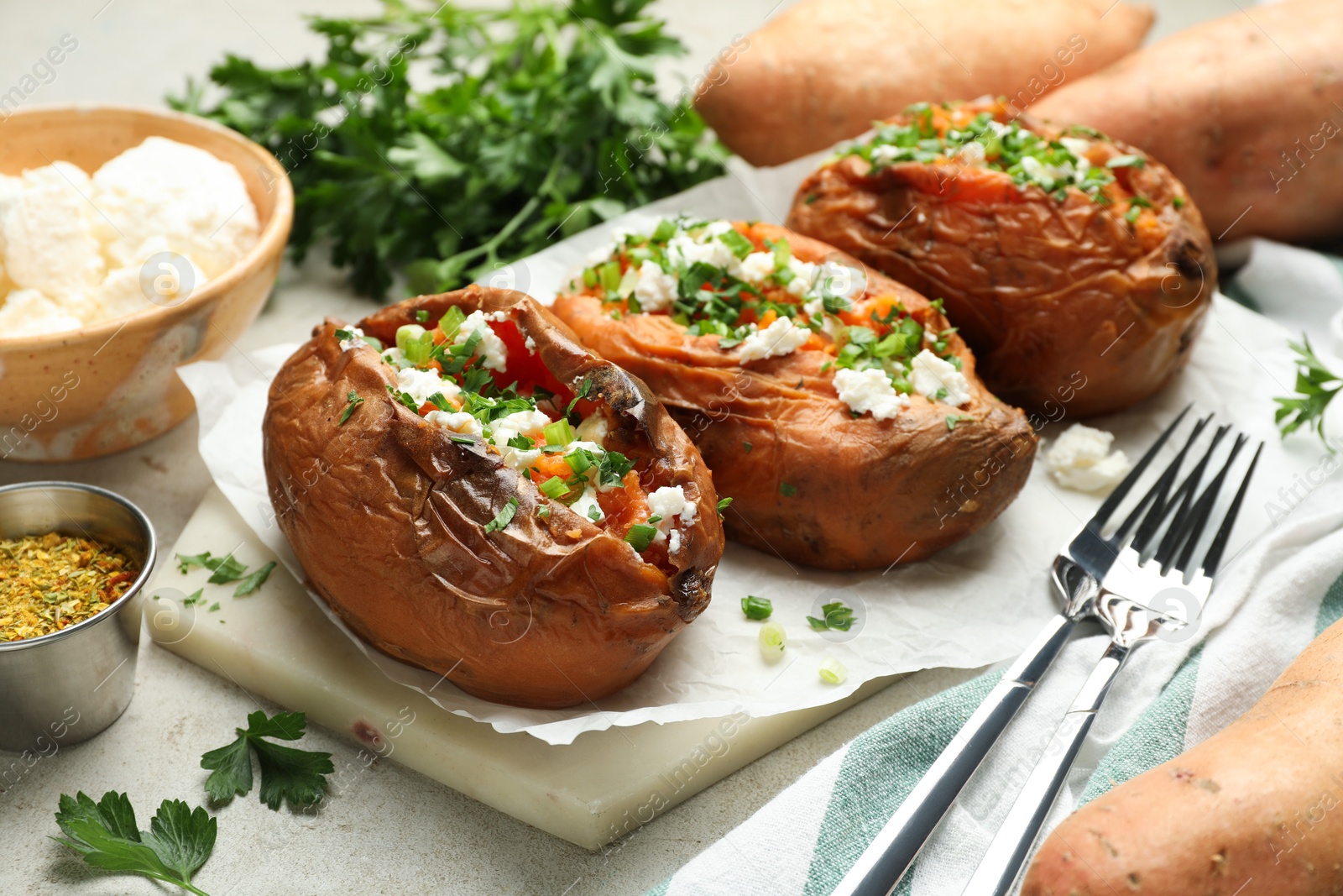 Photo of Tasty cooked sweet potatoes with feta cheese, green onion and parsley served on gray textured table, closeup