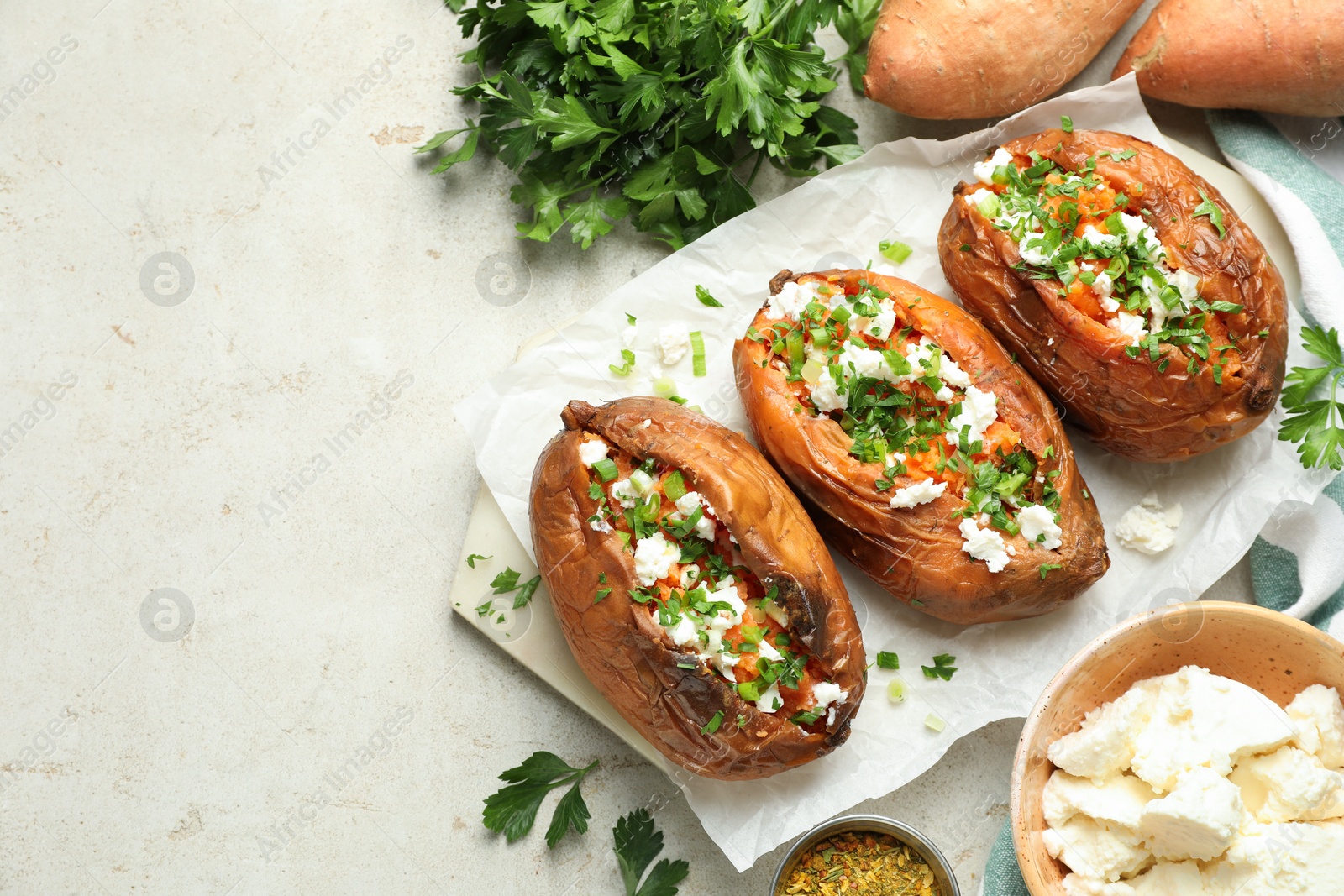 Photo of Tasty cooked sweet potatoes with feta cheese, green onion and parsley on gray textured table, flat lay. Space for text