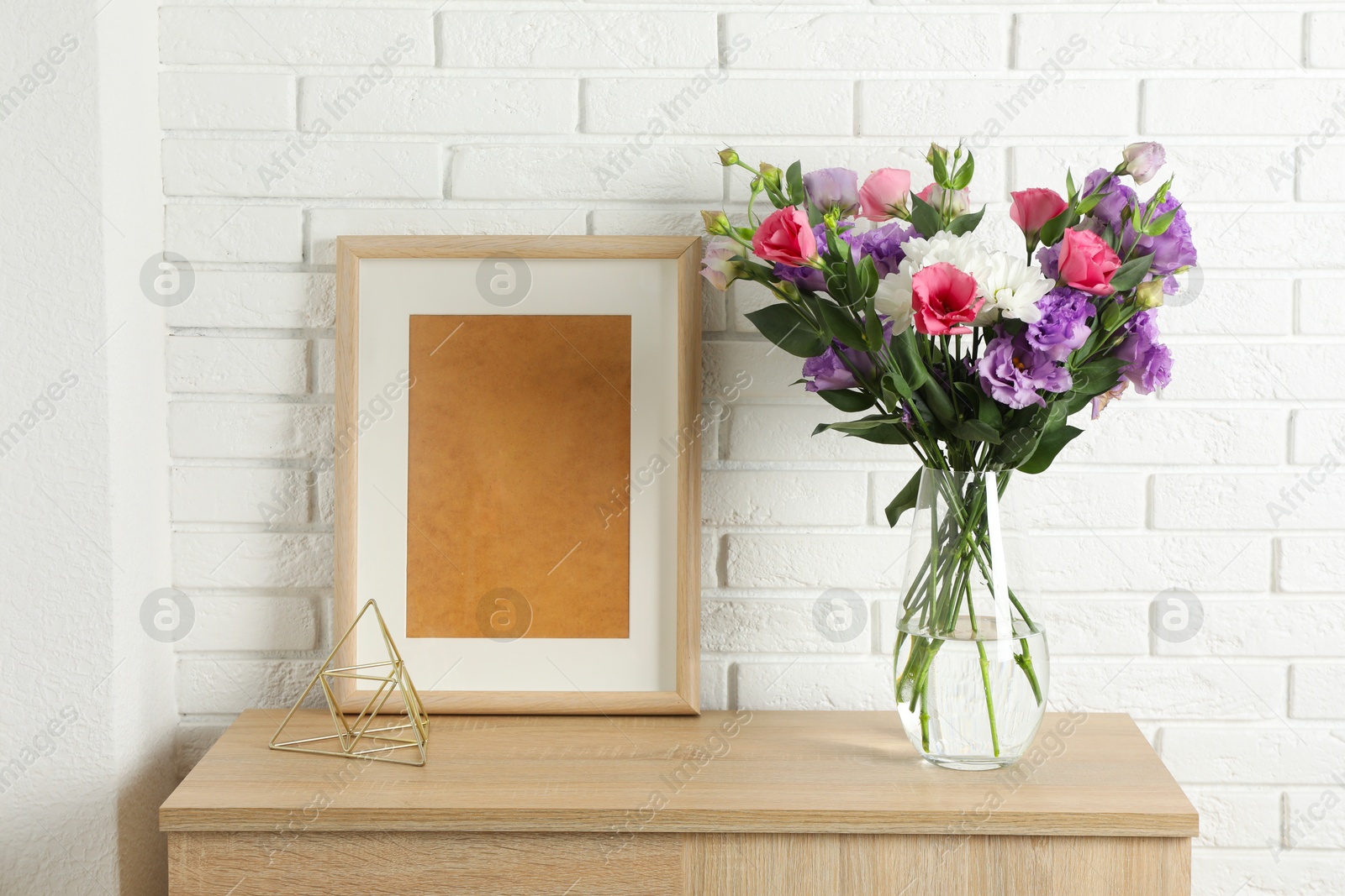 Photo of Vase with beautiful eustoma flowers and picture frame on wooden chest of drawers