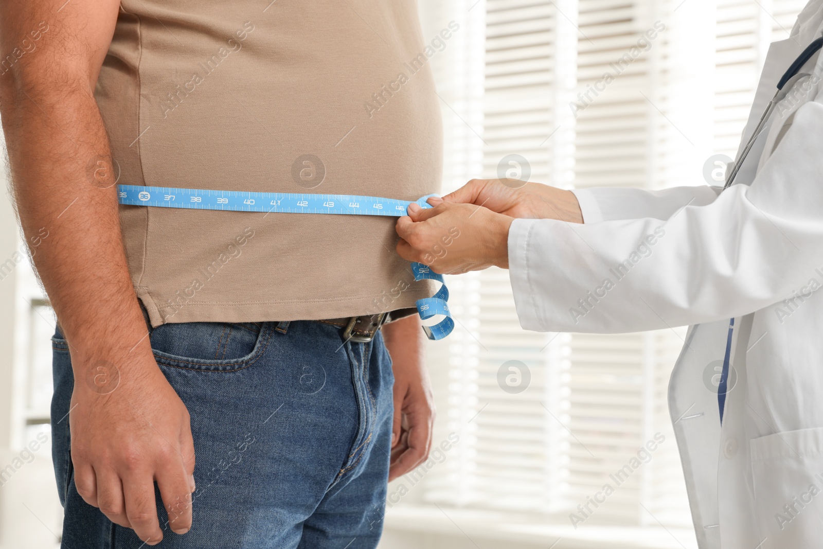 Photo of Nutritionist measuring overweight man's waist with tape in clinic, closeup