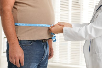 Photo of Nutritionist measuring overweight man's waist with tape in clinic, closeup