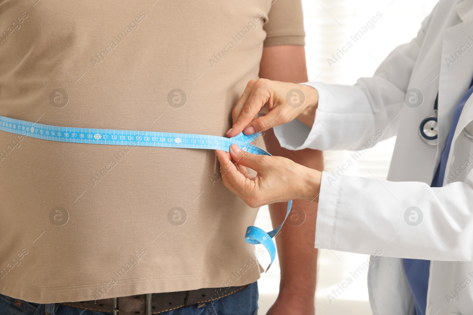 Photo of Nutritionist measuring overweight man's waist with tape in clinic, closeup