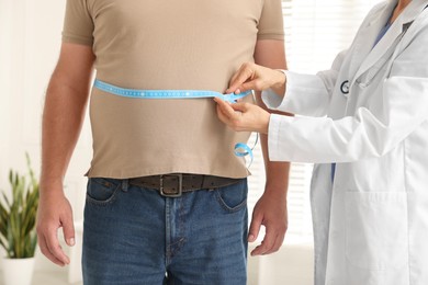 Photo of Nutritionist measuring overweight man's waist with tape in clinic, closeup