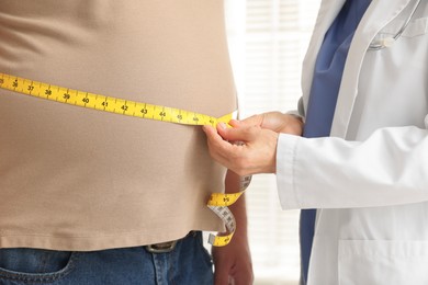 Photo of Nutritionist measuring overweight man's waist with tape in clinic, closeup